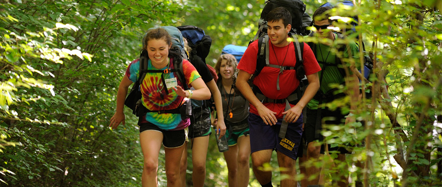 Students hike enthusiastically uphill with backpacks.