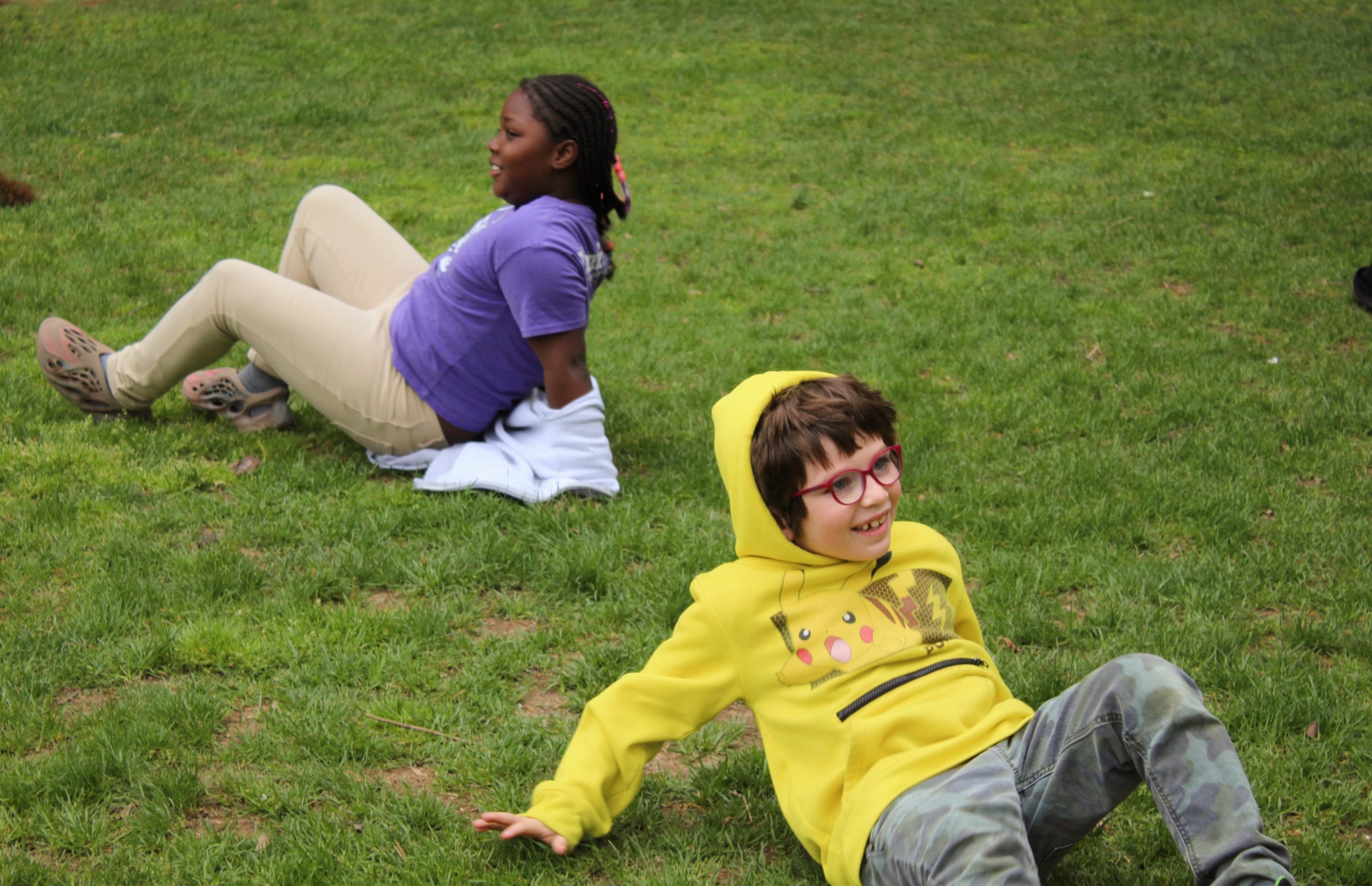 Kids crab-walking smiling. two tutees with a yellow pikachu jacket and purple t-shirt at the 2023 field day
