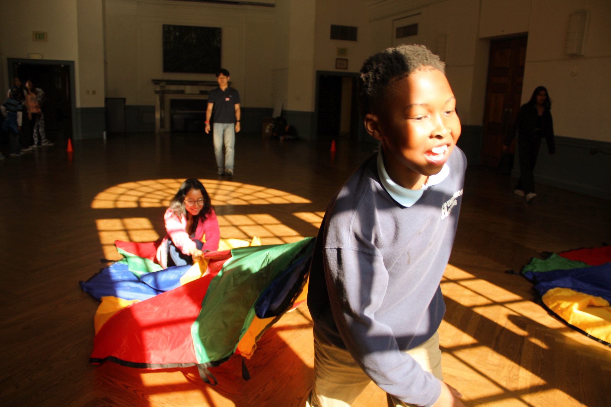 Tutee dragging tutor on a parachute inside the Great Hall at the 2023 field day