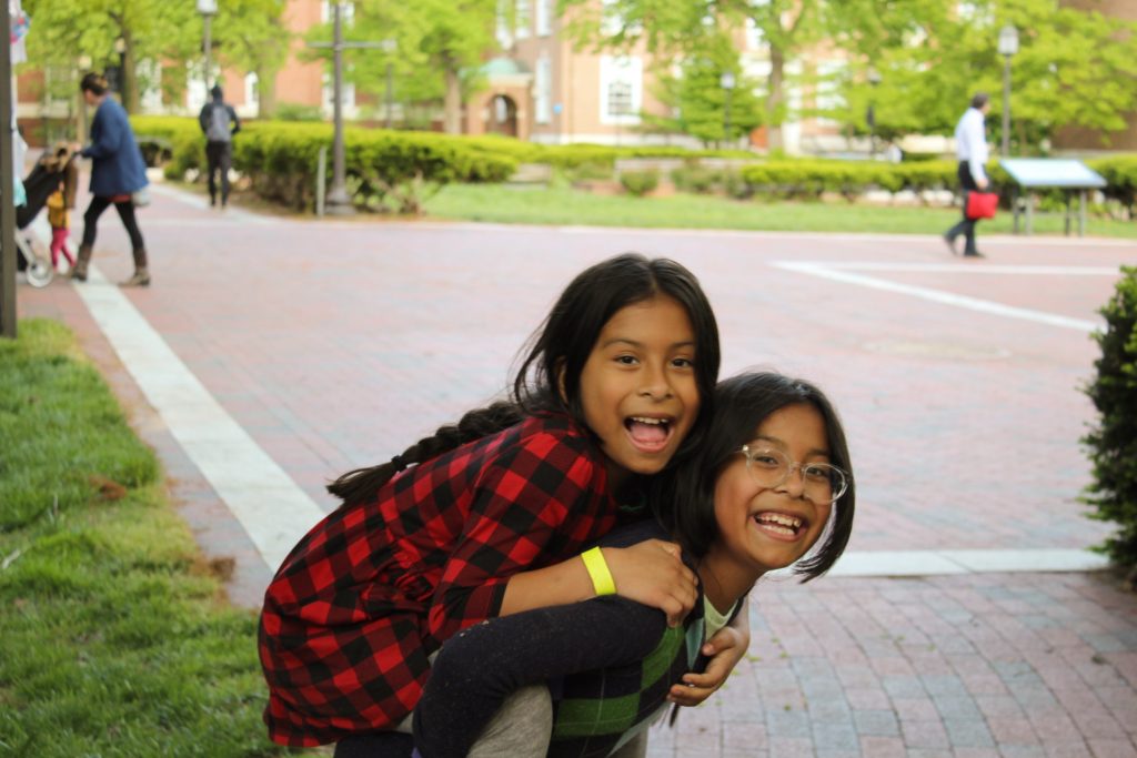 Two tutee sisters smiling giving a piggyback to one another at the 2023 field day