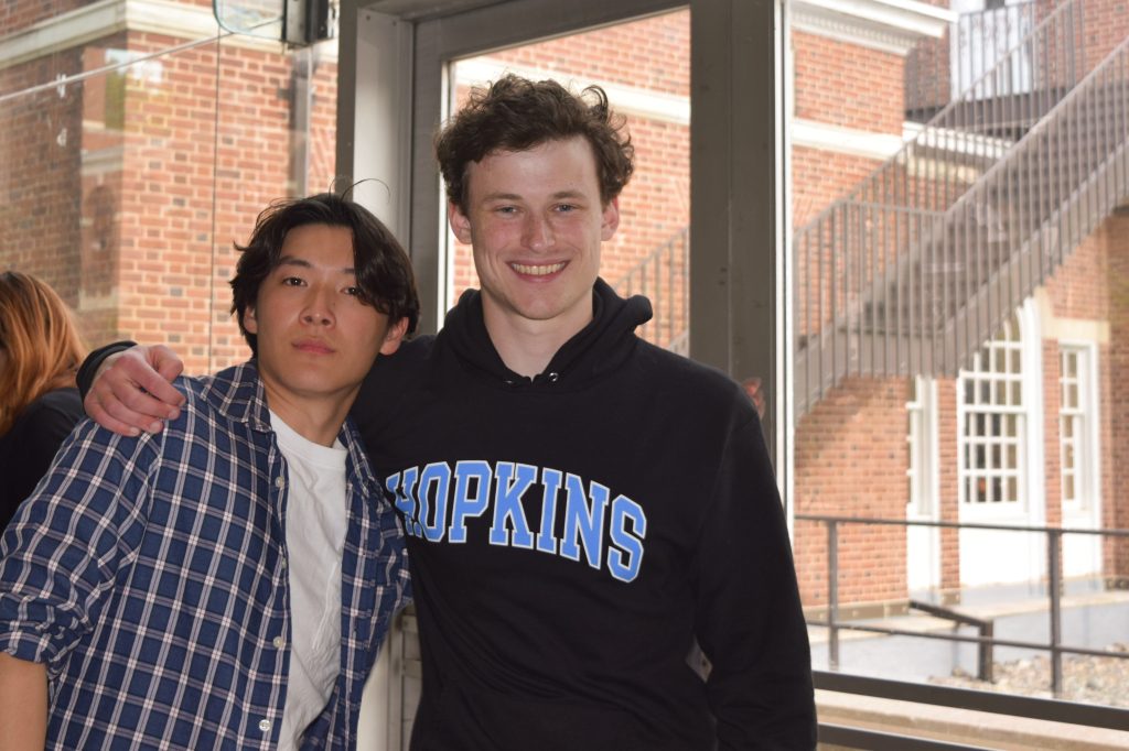 Two tutorial project student workers smiling. One wearing a blue flannel and white t-shirt and the other wearing a black Hopkins hoodie in black