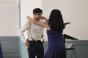 Alec Gonzaga, smiling while receiving a chord from Julie Rivera, CSC staff. Julie is wearing a blue dress and Alec is wearing a white dress shirt.