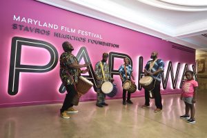 A group of men banging drums in front of the Parkway Theatre