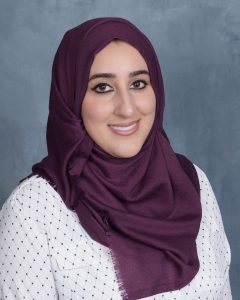 Nusaybah smiling wearing a white polka dot shirt and a purple hijab