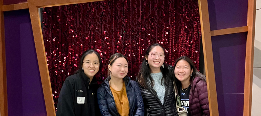 Stacey Tang and friends smiling outside of a shiny red background