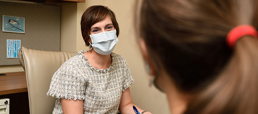 A female health care provider wearing a surgical mask speaks to a student