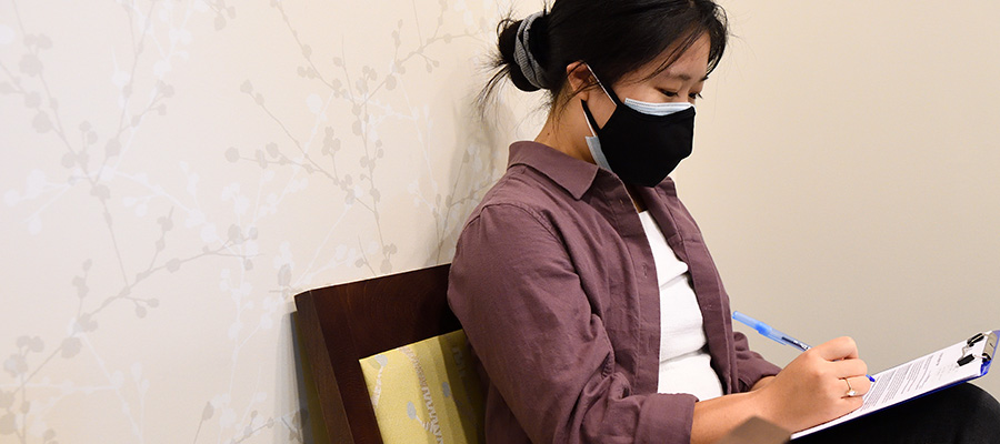 A patient wearing a face mask sitting in a chair and filling out a form