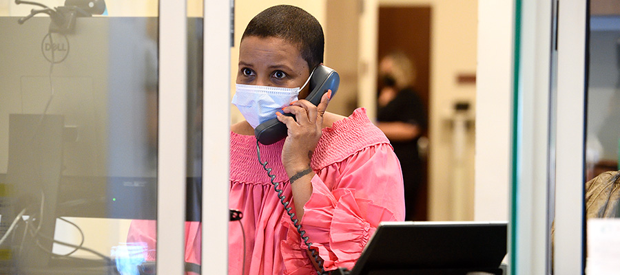 A female receptionist wearing a face mask answers a phone